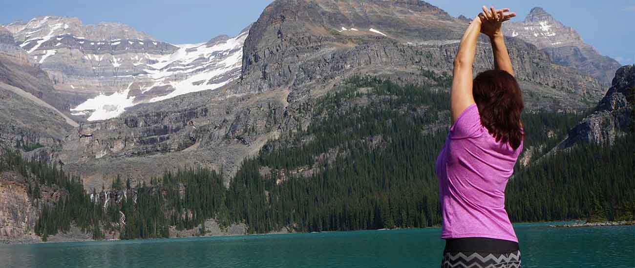 woman in a side bend stretch while looking at a glacier lake and mountains in canada
