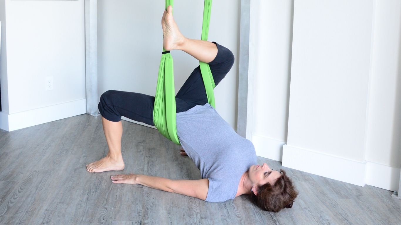 woman doing aerial yoga pigeon pose in supine with a green hammock