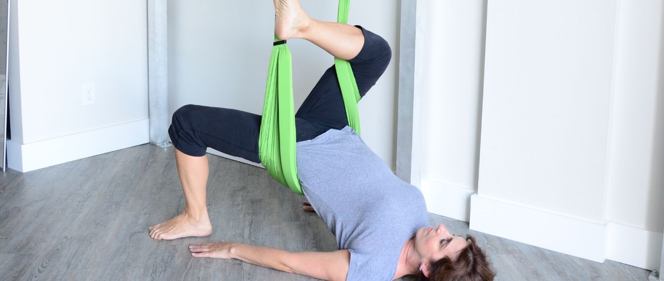 woman doing aerial yoga pigeon pose in supine with a green hammock
