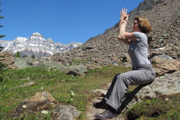 woman wearing grey sits and does eagle pose arms stretches while walking